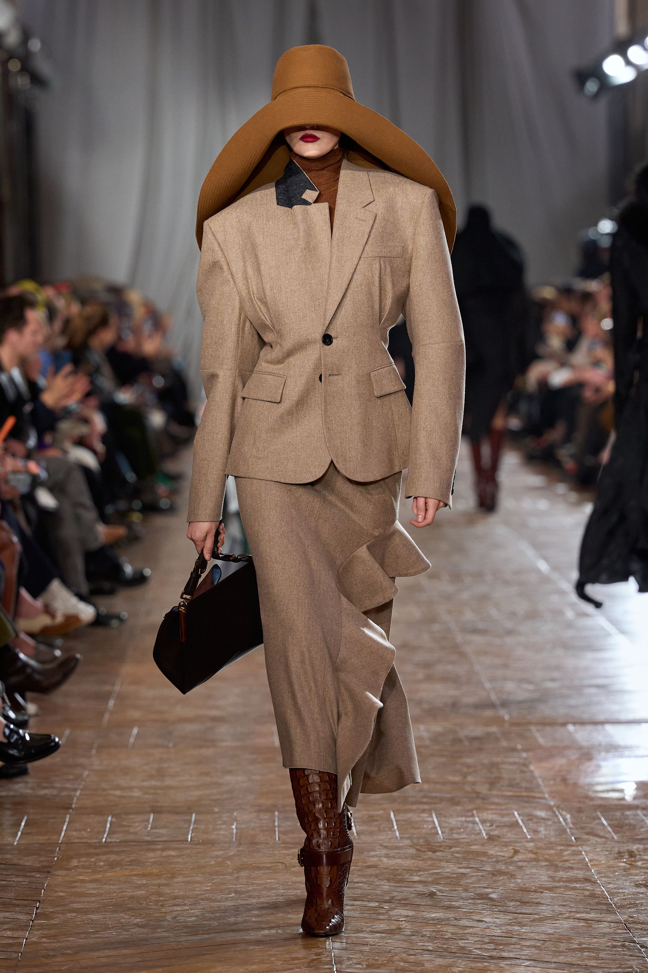 Lanvin 本季回归品牌最经典的巴黎女性气质：结构精准的西装、收腰裙装、深色羊毛套装与戏剧性大檐帽形成一种冷静而克制的奢华。柔软褶皱、细腰剪裁与高靴搭配营造出带有1930年代气息的摩登贵族感，同时通过金属亮片与垂坠流苏礼服让夜晚部分显得华丽而锋利。整场秀像一场巴黎旧贵族的时装电影，优雅却不失力量-顽石频道趋势研究